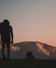 silhouette of man walking along field leading to mountain