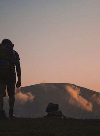 silhouette of man walking along field leading to mountain