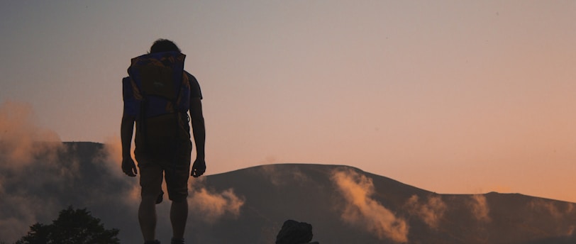 silhouette of man walking along field leading to mountain