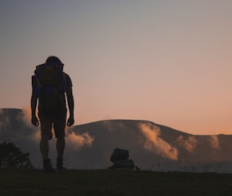 silhouette of man walking along field leading to mountain