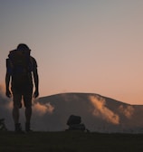 silhouette of man walking along field leading to mountain