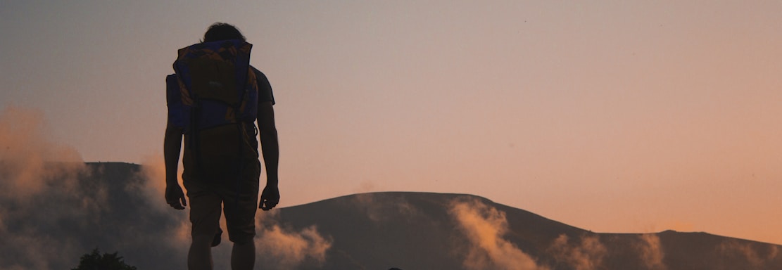 silhouette of man walking along field leading to mountain