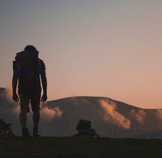 silhouette of man walking along field leading to mountain