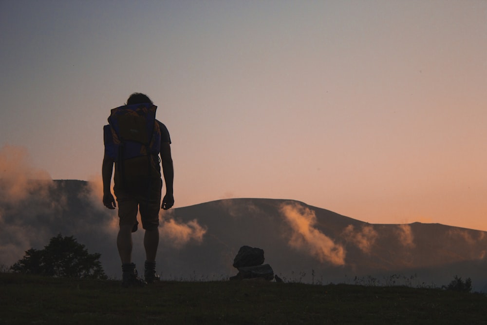 silhouette of man walking along field leading to mountain