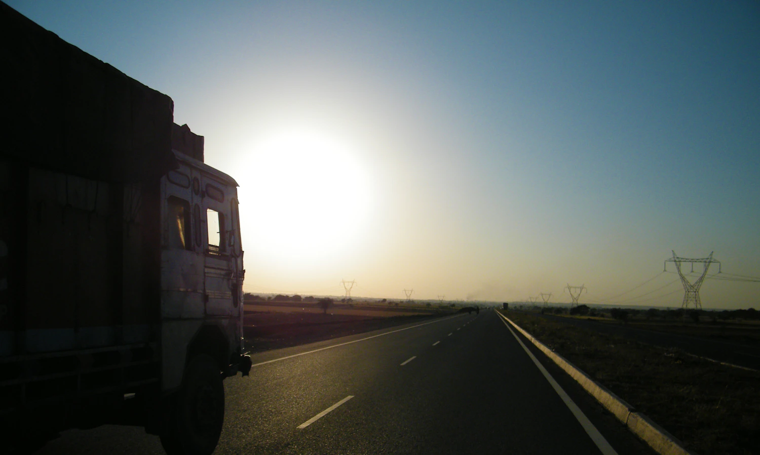 A truck traveling an open road toward the sunset
