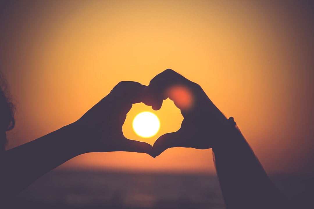 Hands in the silhouette of a heart outline the setting sun on a beach