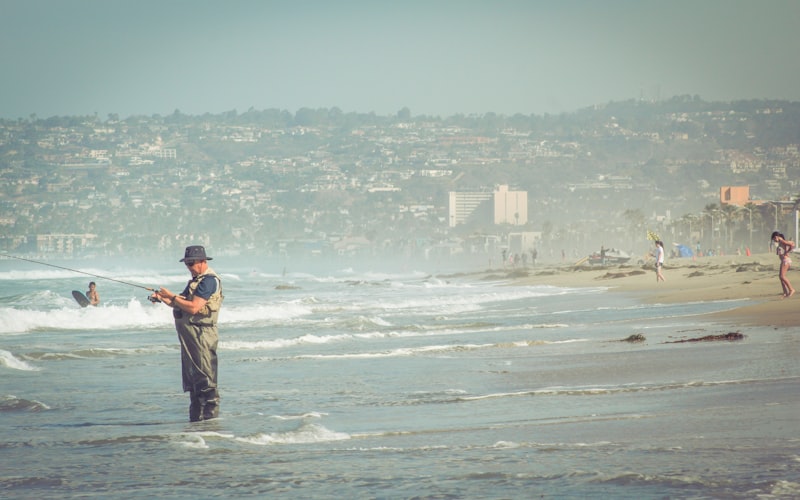 a man standing on the shallow part of the sea and using a fishing rod to fish