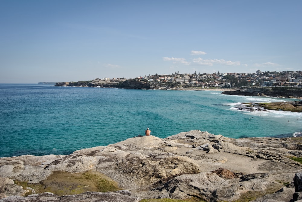 man sitting on rock looking on sea at daytime