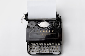 A black and white photo of a vintage typewriter with a sheet of paper, set against a dark gothic backdrop.