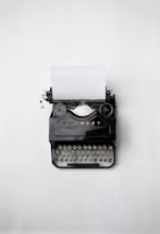 A black and white photo of a vintage typewriter with a sheet of paper, set against a dark gothic backdrop.