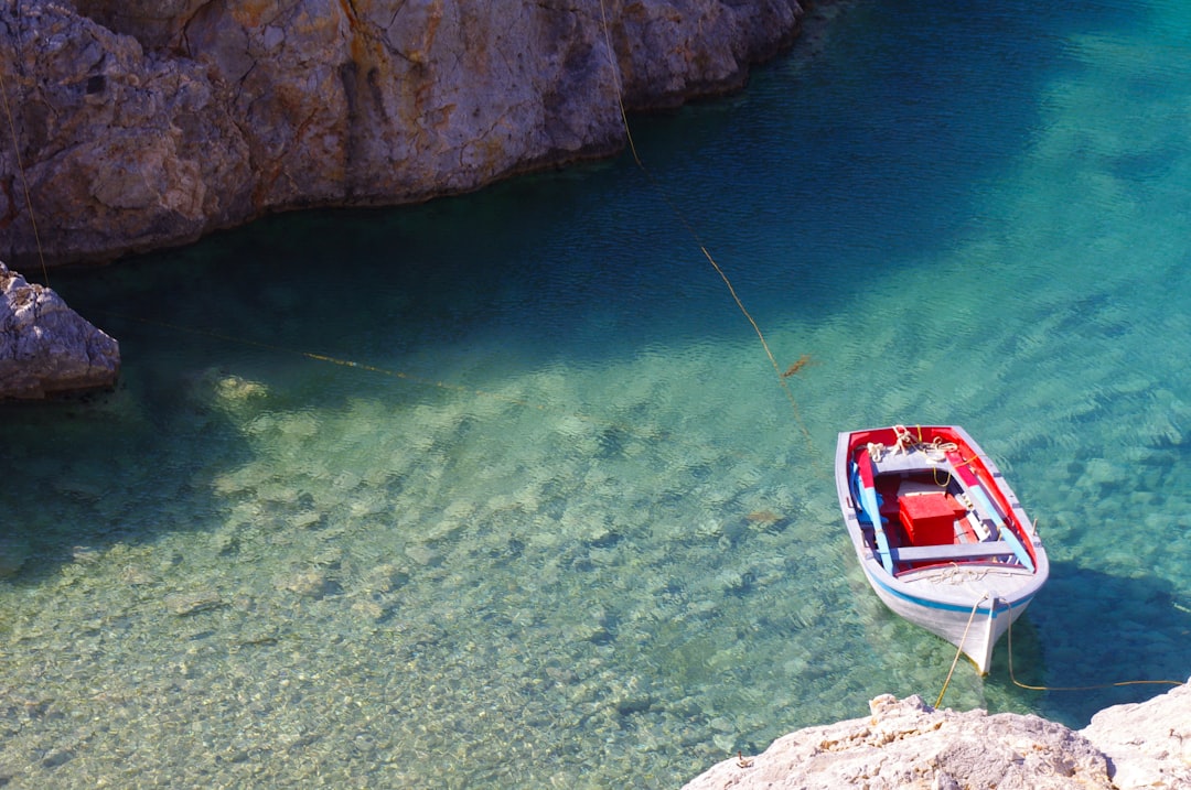 white and red boat toy docked on brown rock,