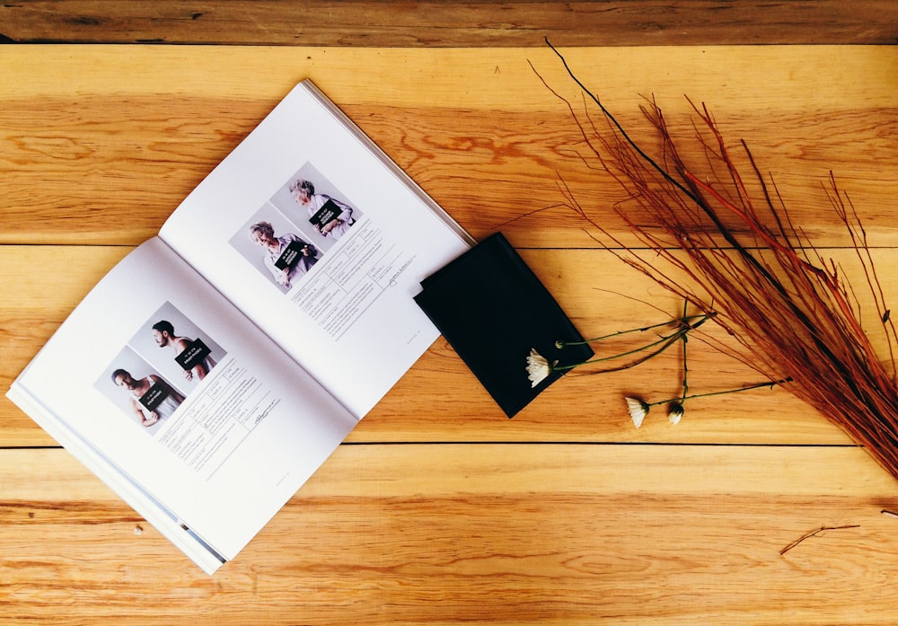 A book of headshots, a black paper, and old dried flowers on a wooden surface