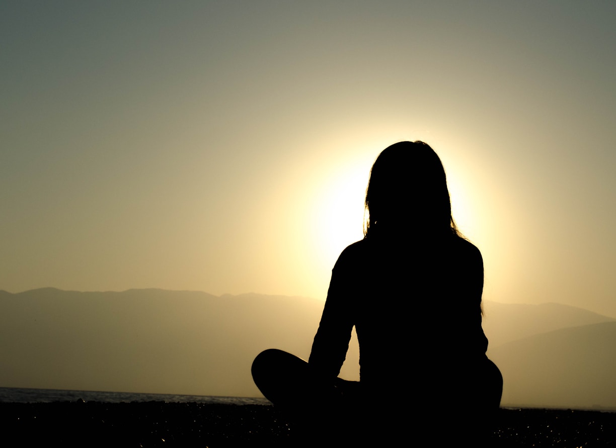 A peaceful scene of a person meditating outdoors at sunrise, symbolizing personal well-being and balance.