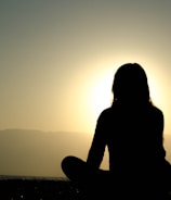 Silhouettes of individuals meditating outdoors during sunrise.