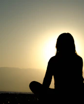 A tranquil outdoor setting with a person meditating at sunrise, embodying devotion.