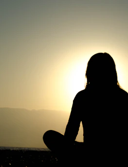 A tranquil outdoor setting with a person meditating at sunrise, embodying devotion.