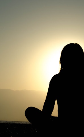 Miss Asera seated cross-legged on a mountaintop at dawn, eyes closed in peaceful meditation.
