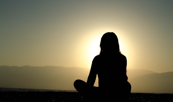 A peaceful scene of a person sitting cross-legged near a quiet lake at sunrise.