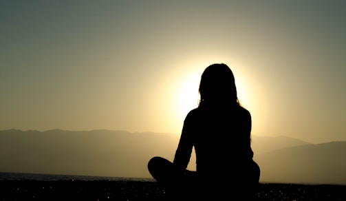 Silhouettes of individuals meditating outdoors during sunrise.