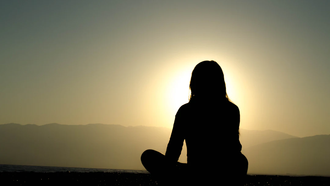 Woman meditating by a lake at sunset
