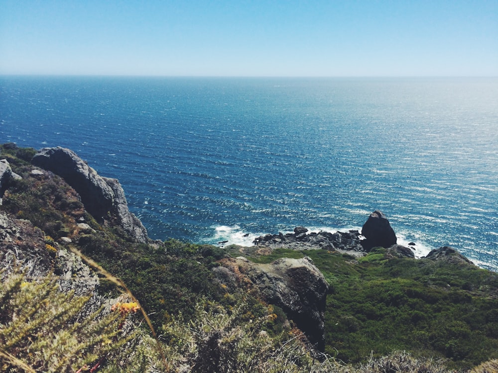 person sitting on cliff near body of water