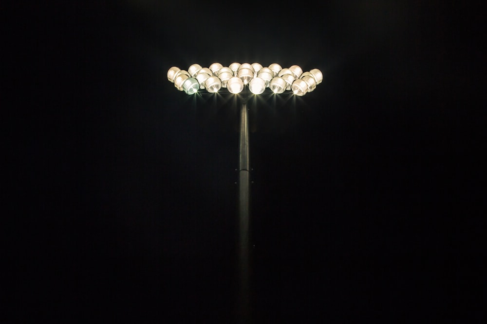 Floodlights shining at the top of a light pole with a pitch black background