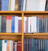 A bookshelf filled with a variety of academic and professional books, arranged neatly in rows. The spines display titles in different languages and cover various topics. Some books are thicker, while others are thinner, showing diversity in publishing styles.