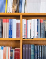 A bookshelf filled with a variety of academic and professional books, arranged neatly in rows. The spines display titles in different languages and cover various topics. Some books are thicker, while others are thinner, showing diversity in publishing styles.