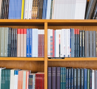A bookshelf filled with a variety of academic and professional books, arranged neatly in rows. The spines display titles in different languages and cover various topics. Some books are thicker, while others are thinner, showing diversity in publishing styles.