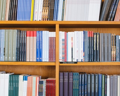 A bookshelf filled with a variety of academic and professional books, arranged neatly in rows. The spines display titles in different languages and cover various topics. Some books are thicker, while others are thinner, showing diversity in publishing styles.