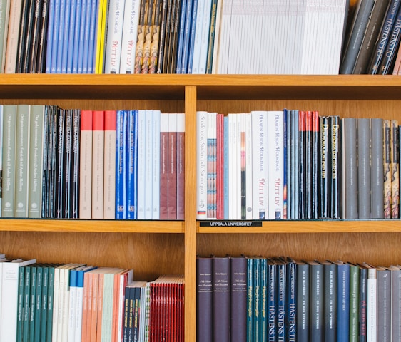 A bookshelf filled with a variety of academic and professional books, arranged neatly in rows. The spines display titles in different languages and cover various topics. Some books are thicker, while others are thinner, showing diversity in publishing styles.