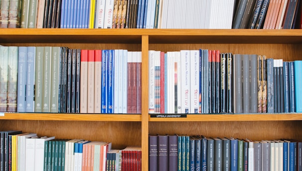 A bookshelf filled with a variety of academic and professional books, arranged neatly in rows. The spines display titles in different languages and cover various topics. Some books are thicker, while others are thinner, showing diversity in publishing styles.