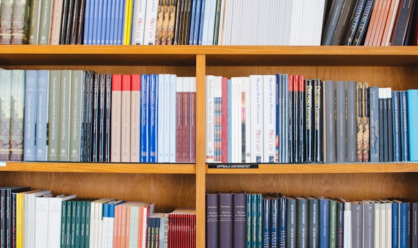 A bookshelf filled with a variety of academic and professional books, arranged neatly in rows. The spines display titles in different languages and cover various topics. Some books are thicker, while others are thinner, showing diversity in publishing styles.