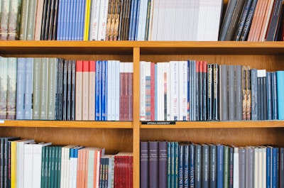 A bookshelf filled with a variety of academic and professional books, arranged neatly in rows. The spines display titles in different languages and cover various topics. Some books are thicker, while others are thinner, showing diversity in publishing styles.