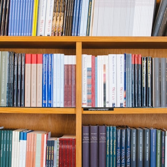 A bookshelf filled with a variety of academic and professional books, arranged neatly in rows. The spines display titles in different languages and cover various topics. Some books are thicker, while others are thinner, showing diversity in publishing styles.