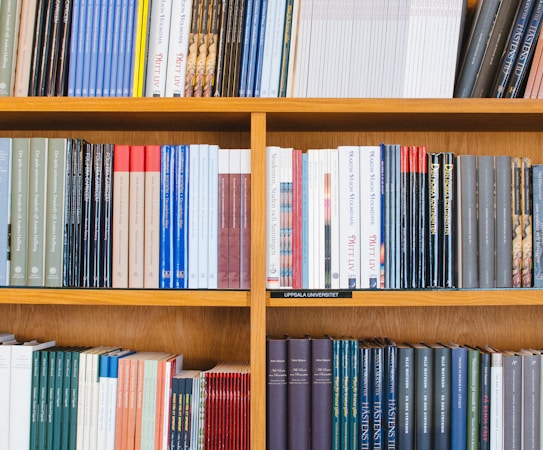 A bookshelf filled with a variety of academic and professional books, arranged neatly in rows. The spines display titles in different languages and cover various topics. Some books are thicker, while others are thinner, showing diversity in publishing styles.