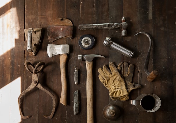 clothes iron, hammer, axe, flashlight and pitcher on brown wooden table