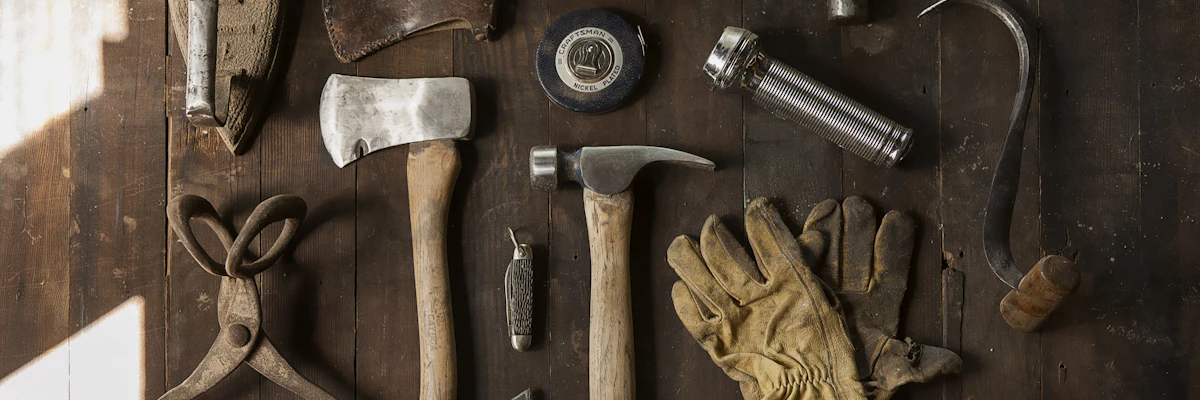 Vintage tools including an axe, hammer, gloves, and metal implements on dark wooden planks