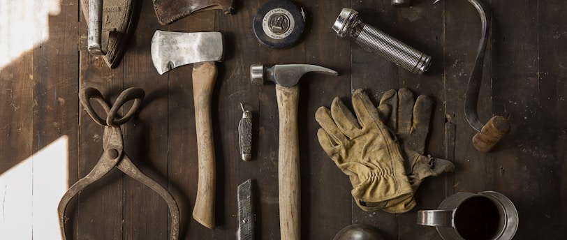 clothes iron, hammer, axe, flashlight and pitcher on brown wooden table