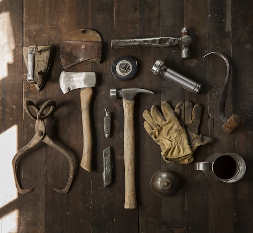clothes iron, hammer, axe, flashlight and pitcher on brown wooden table