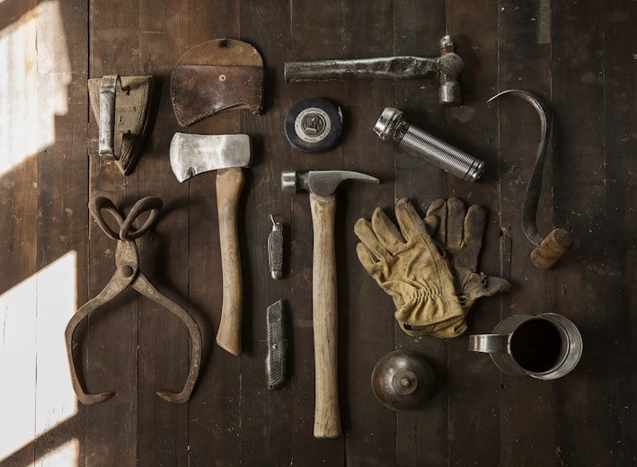 clothes iron, hammer, axe, flashlight and pitcher on brown wooden table