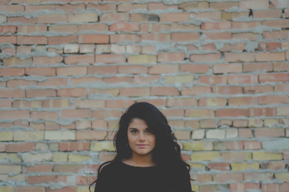 tilt shift lens photography of woman standing near brown brick wall