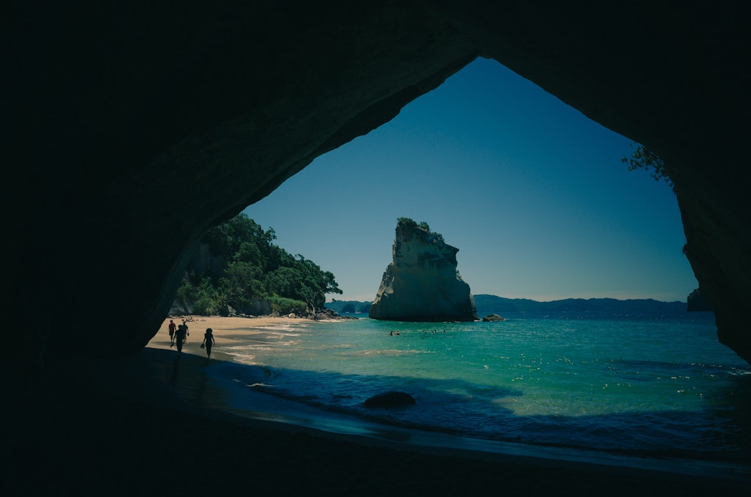 people walking on seashore near body of water, View from a beach cave