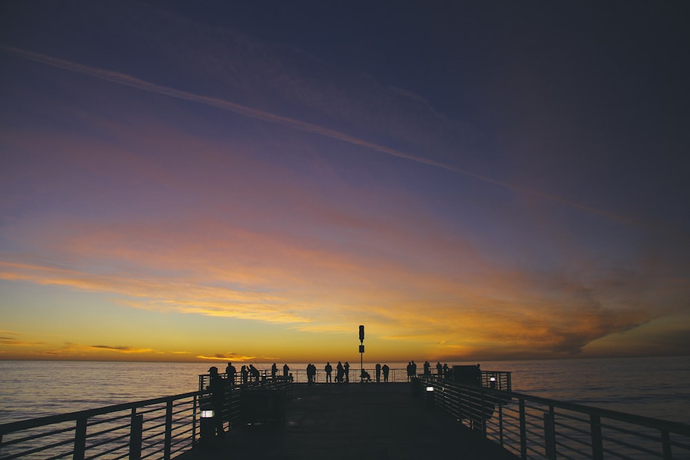 silhouette of people on dock near body of water during golden hour