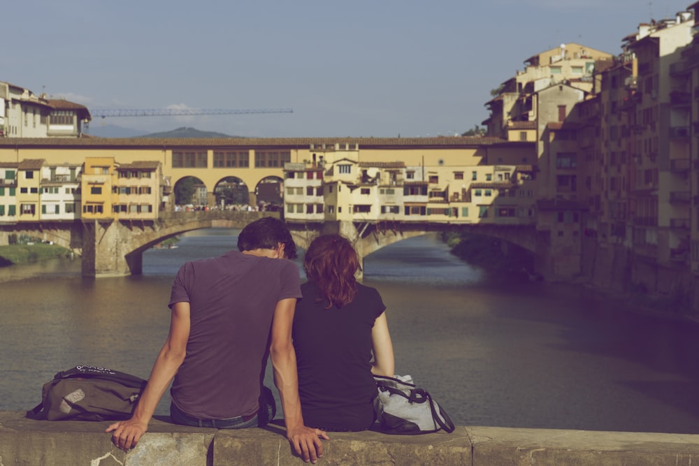 uomo e donna che si siedono insieme davanti allo specchio d'acqua durante il giorno