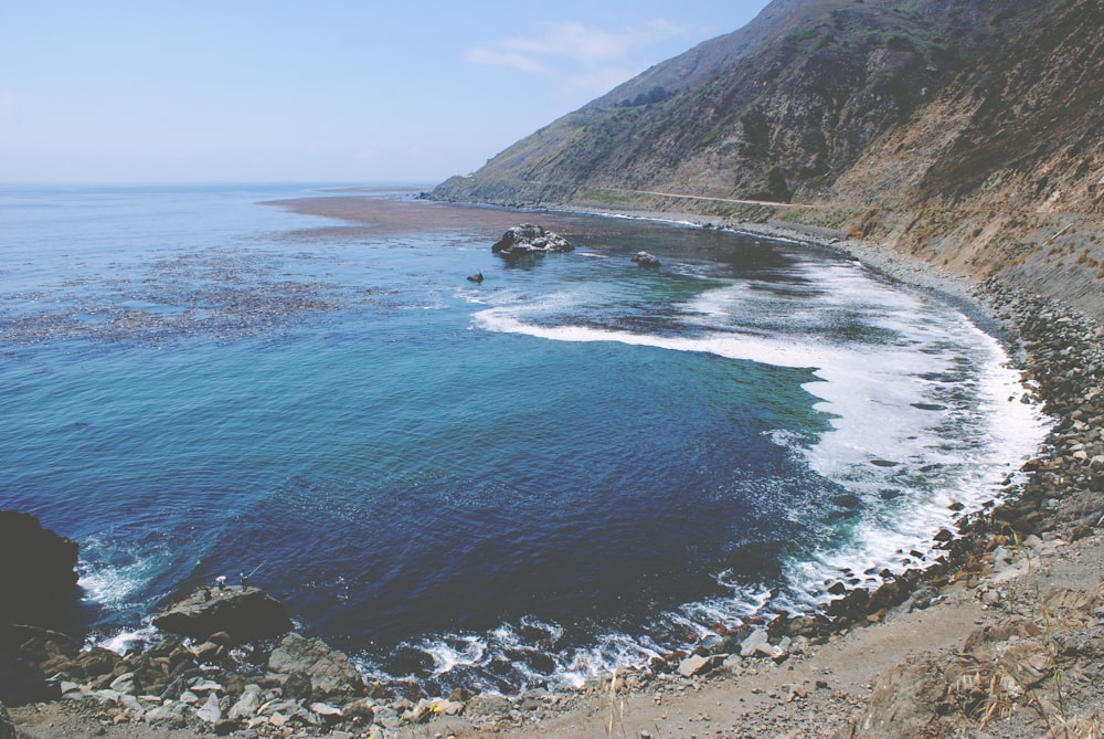 seashore near mountain under cloudy sky