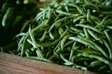 A wooden crate filled with fresh green beans, neatly piled with some lying over the edge. The green beans vary in size and have a natural sheen, indicating freshness.