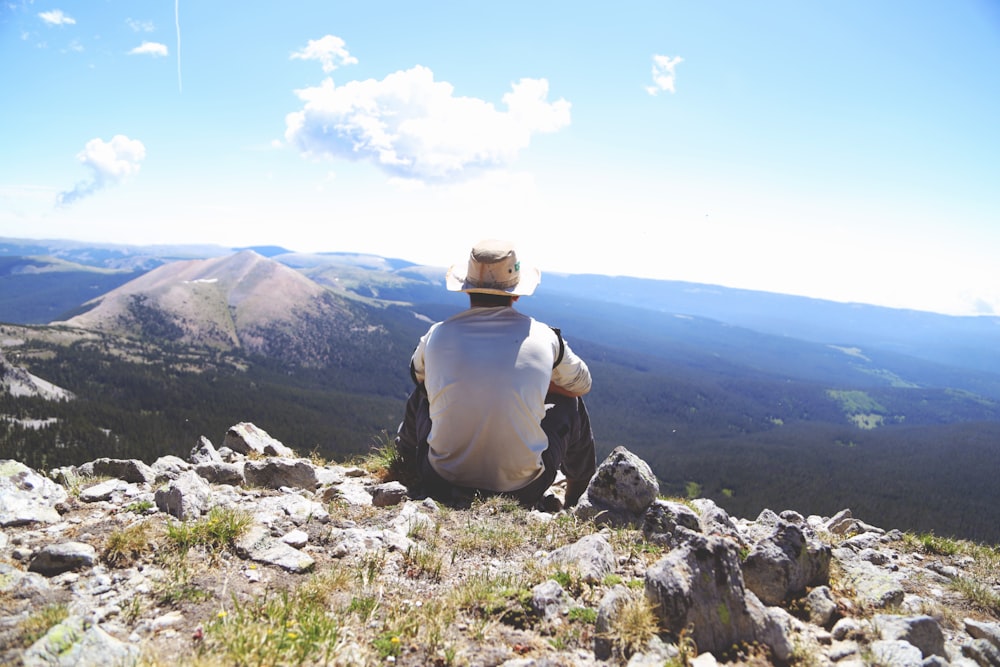 person sitting on a gray rock watching over a mountain