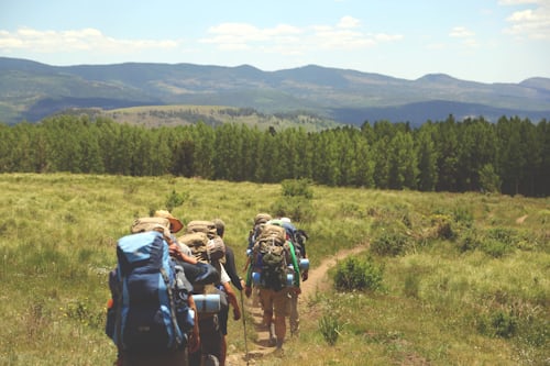 A group of hikers wearing backpacks walking towards a mountain