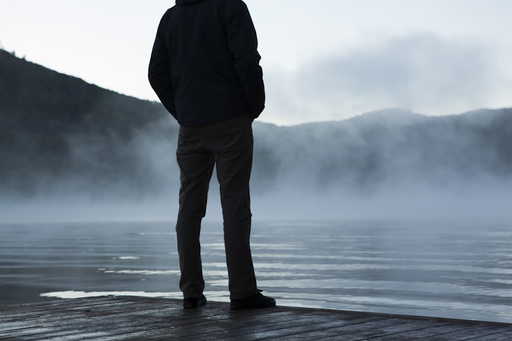 白い空の下、水面を向いて立っている男